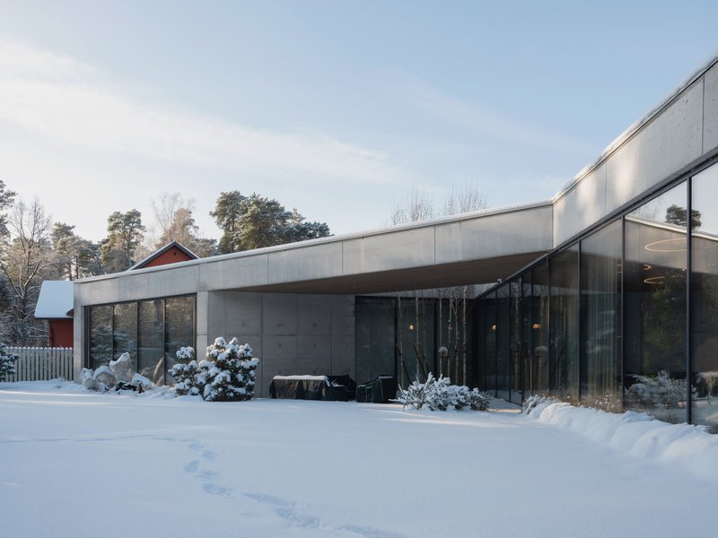 Concrete facade with floor-to-ceiling glass and curving roofline in a snowy garden setting