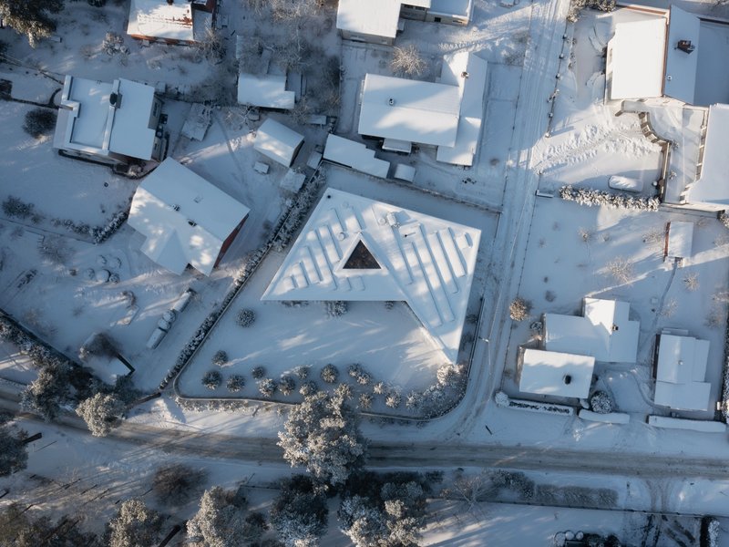 Aerial view of the triangular roof with ribbed skylights nestled among snow-covered residential buildings and frosted trees
