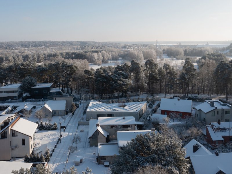 Elevated view of the sawtooth roof form set within a residential neighborhood bordered by pine forest under winter light