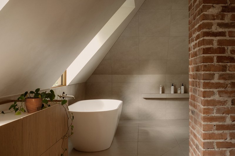 Freestanding bathtub beneath a linear skylight alongside an exposed brick column