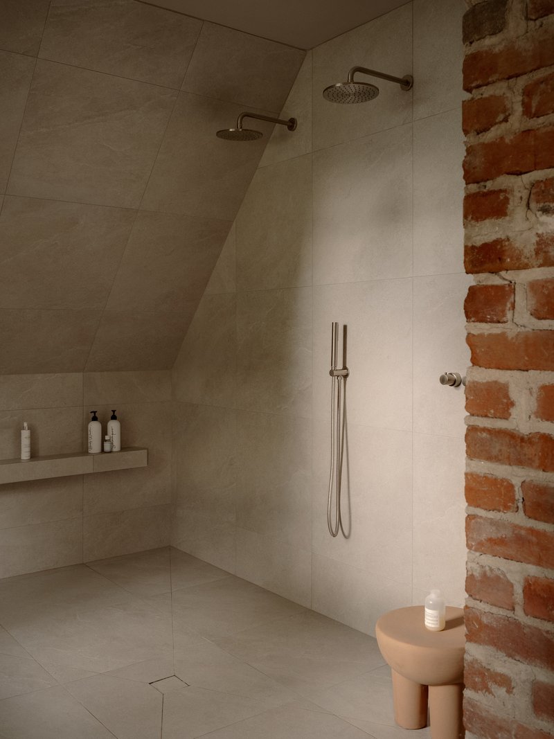 Shower enclosure with dual rainfall heads and exposed brick wall alongside large format stone tiles