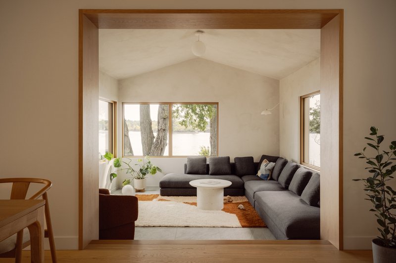 Living room framed by timber portal with vaulted white ceiling and sectional sofa facing lakeside windows