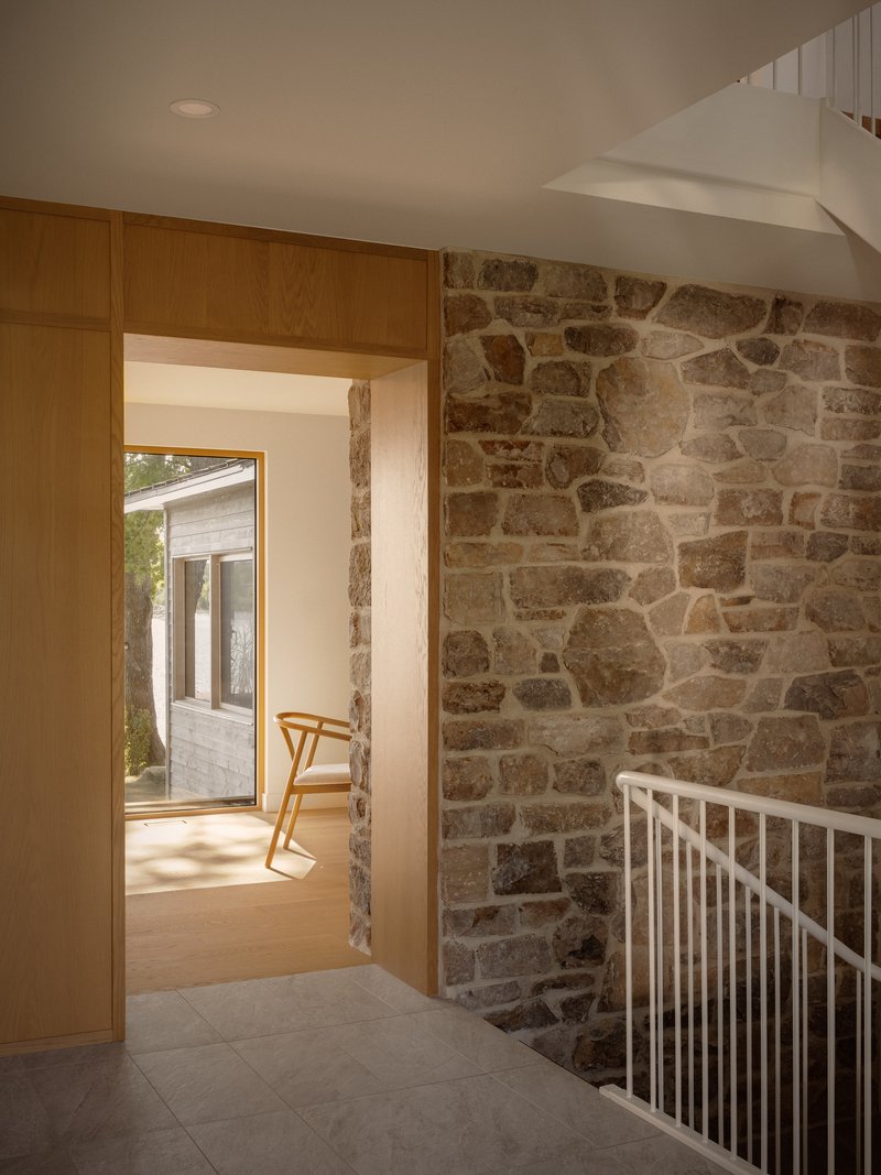Stairwell landing with exposed stone wall and timber-framed doorway opening to exterior deck beyond