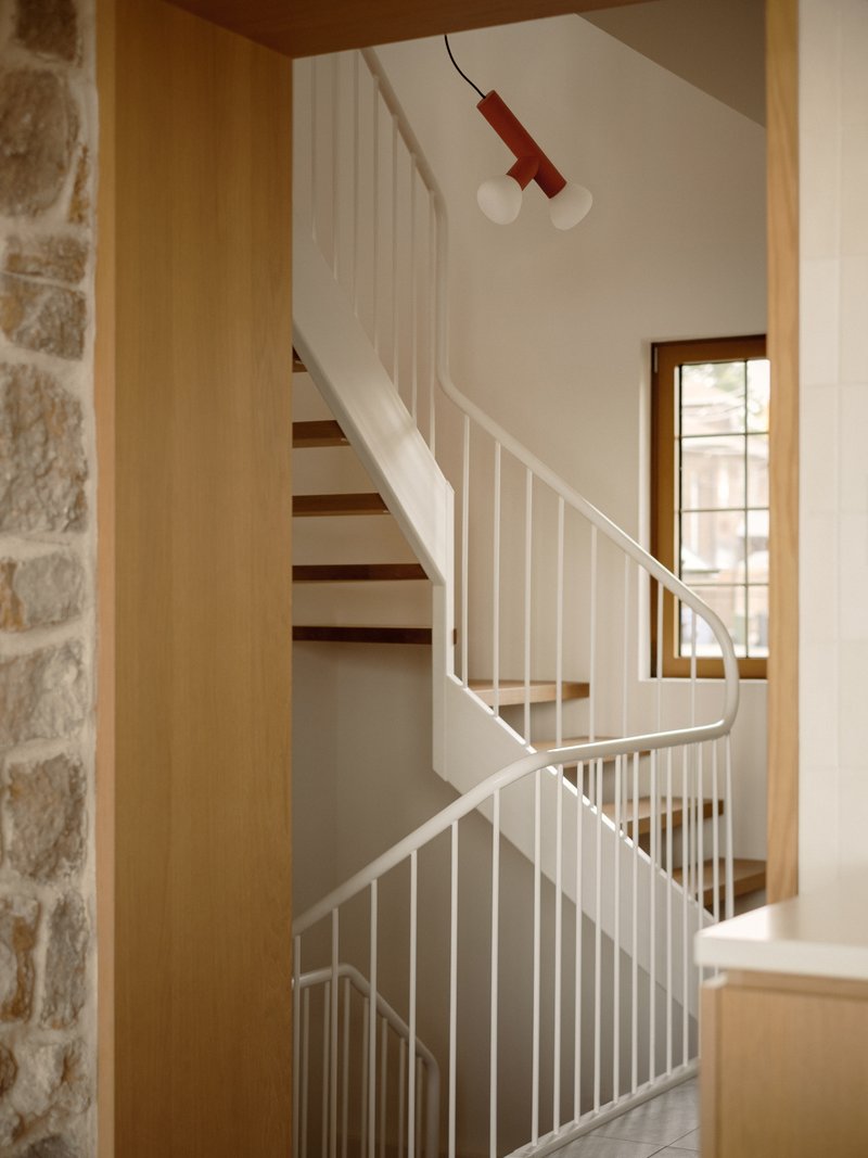 Timber and white steel staircase with vertical balustrade and exposed stone wall at entry