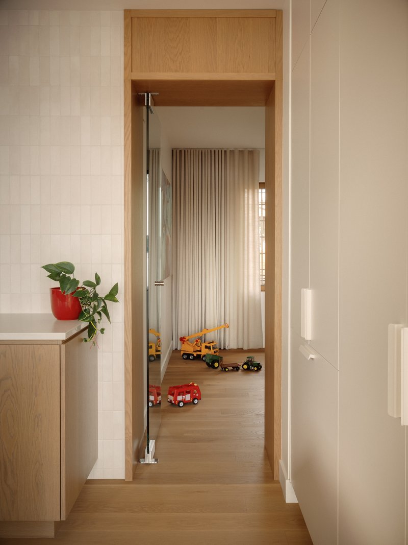 View through oak-lined doorway into bedroom with fluted curtain and toy vehicles on floor