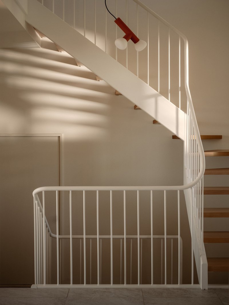 Curved staircase with white metal balustrade and timber treads beneath a red pendant light