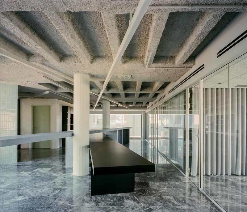 Interior workspace with exposed coffered concrete ceiling, white columns, black tables and marble flooring