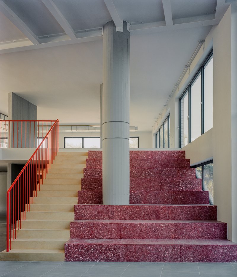 Lobby staircase with red terrazzo treads, light wood risers, red metal railing and central cylindrical column