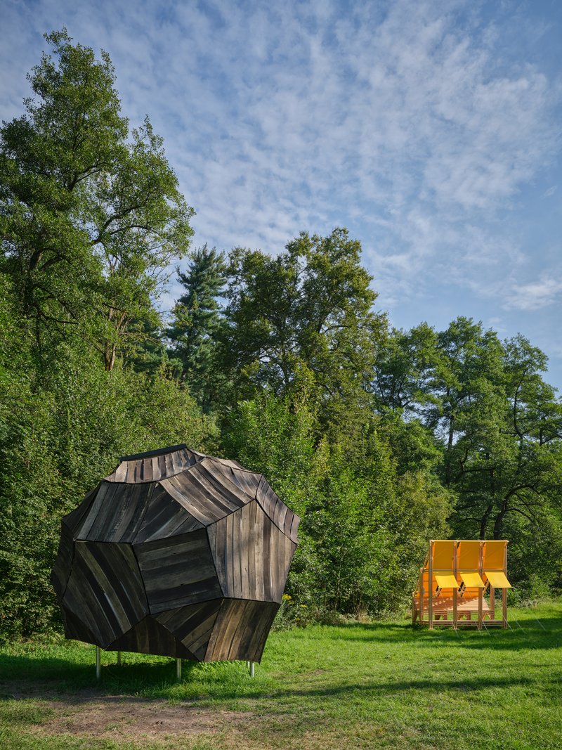 Weathered timber geodesic pavilion on stilts with yellow fabric canopy structure in adjacent clearing