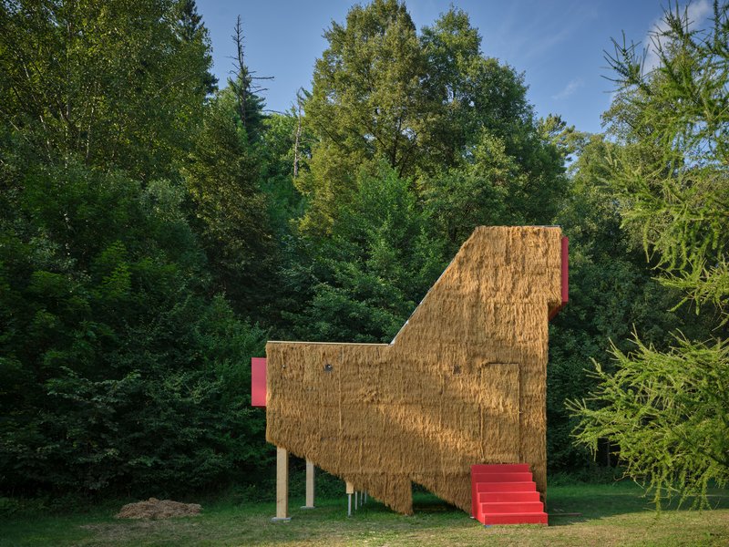 Profile view of the elevated straw bale structure showing angular roofline and red access stair