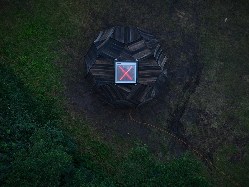 Drone view of the faceted timber pavilion with illuminated red core at dusk
