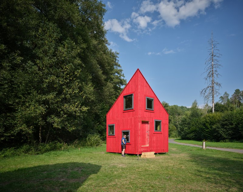 Red clad dwelling with peaked roof and a visitor standing in the doorway on a sunny day