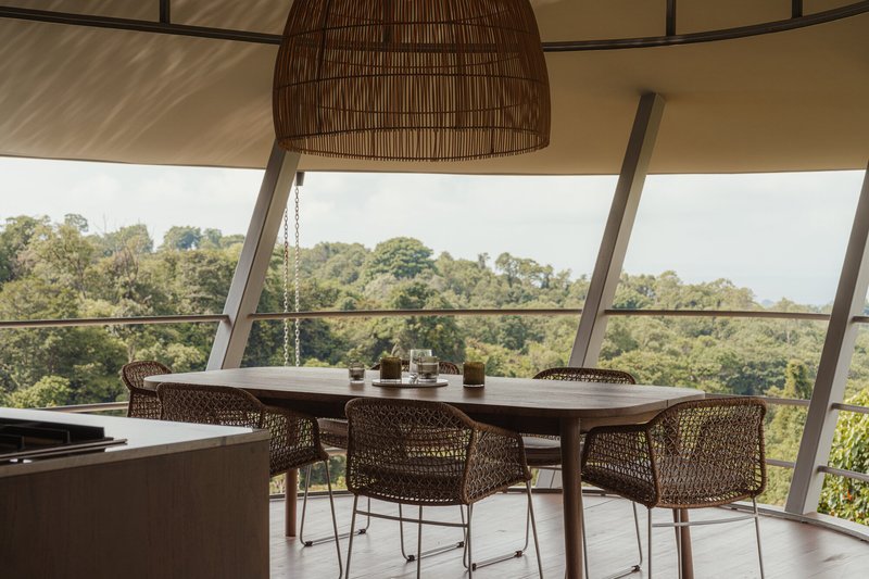 Kitchen and dining area with a long timber table and cane chairs framed by the curved glass wall