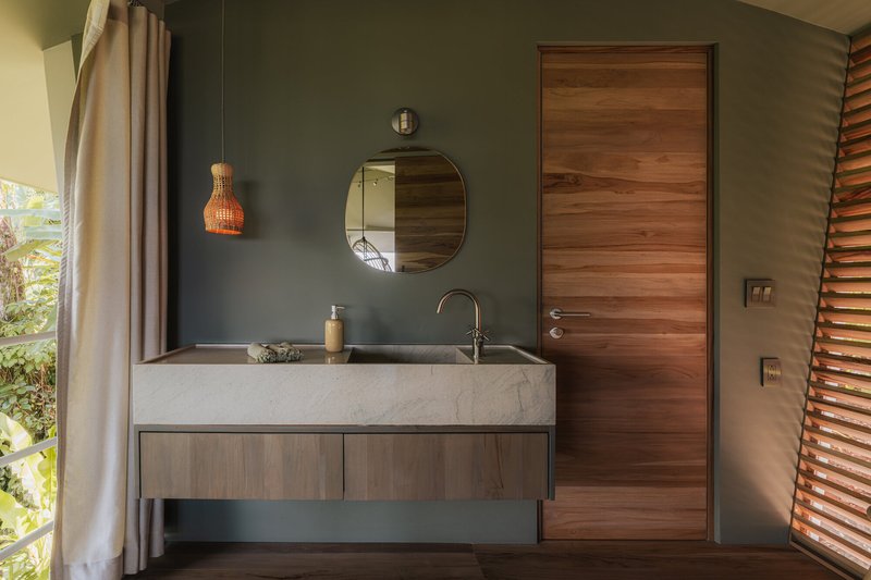 Bathroom with a stone sink, dark green wall and a timber door beside louvered shutters