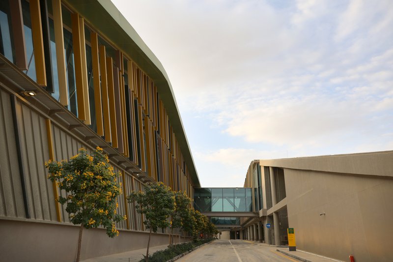 Curved facade with vertical timber fins and corrugated metal cladding beside a glazed connector volume at dusk