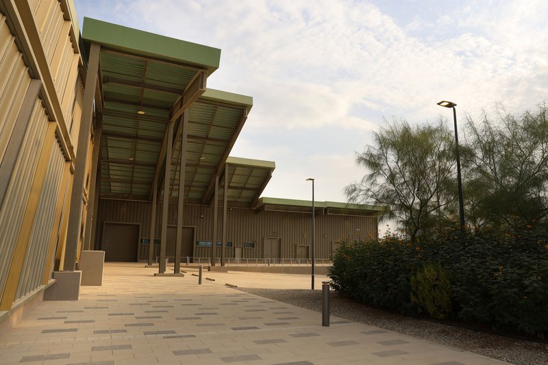 Exterior plaza with paver surface beneath projecting green canopies supported by slender vertical columns
