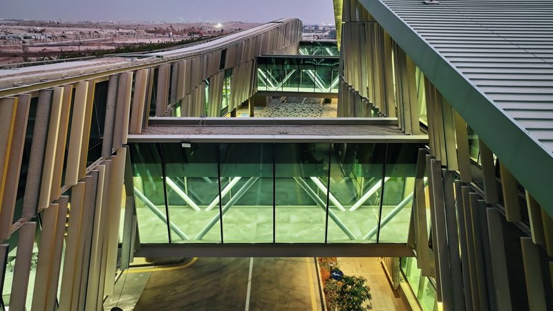 Glass bridge with geometric green tinted glazing flanked by vertical metal louvres at twilight