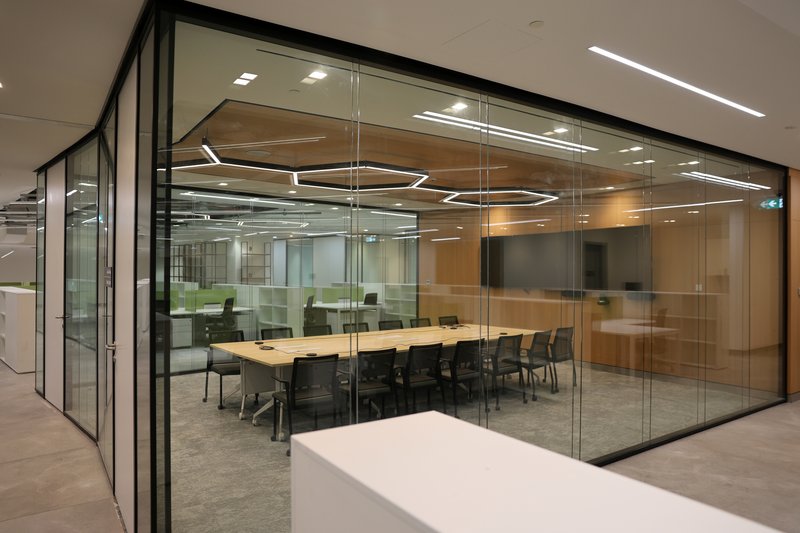 Glass-enclosed meeting room with timber table and black chairs under hexagonal pendant lighting