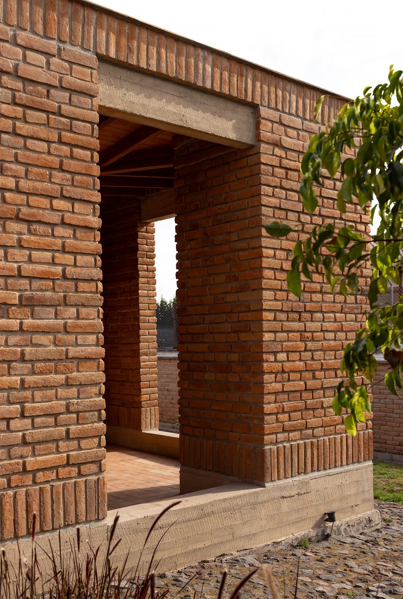Brick passageway with concrete lintel framing a view through to a distant courtyard at dusk