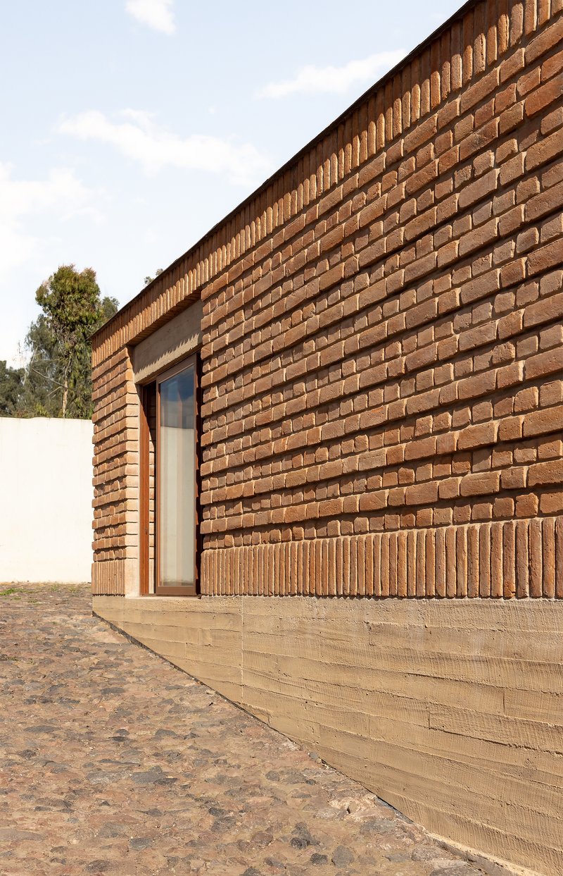 Corner detail of brick wall with recessed concrete base and narrow window set in textured masonry