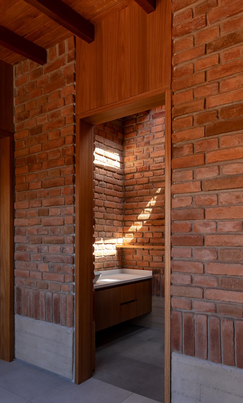 View through timber doorframe into bathroom alcove with brick walls and horizontal light slits