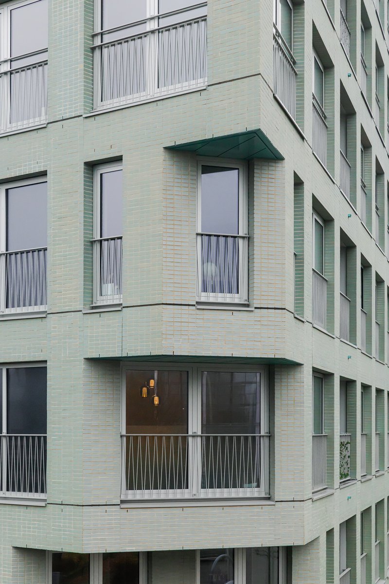 Curved corner balconies with metal railings and pale green tile cladding wrapping the facade in daylight