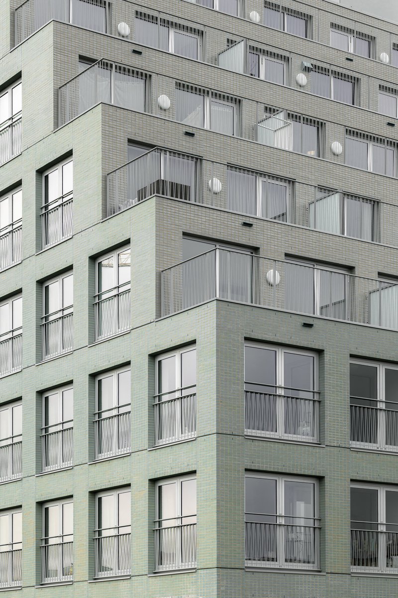 Facade detail showing alternating green and grey brick panels with recessed balconies and floor-to-ceiling windows