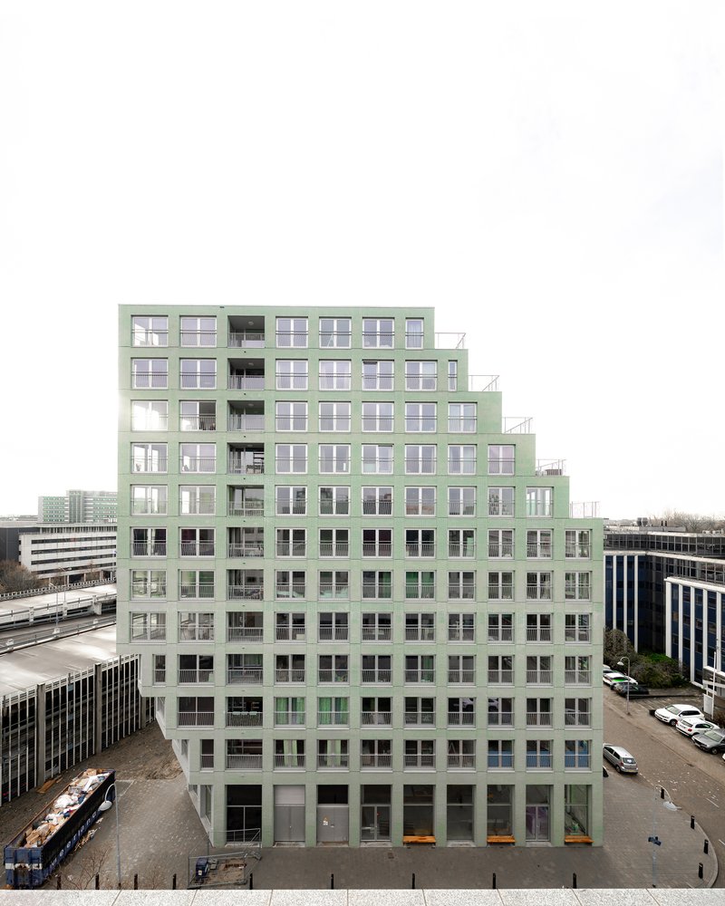 Stepped facade in pale green with recessed balconies viewed from across an adjacent roadway