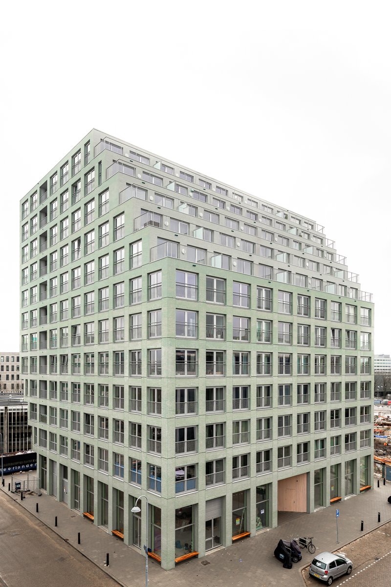Corner elevation of the pale green facade with regular window openings and ground-level street activity