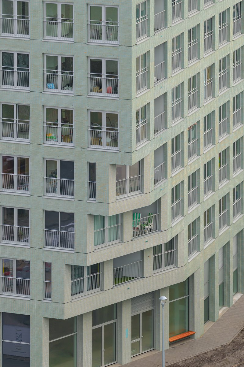 Corner courtyard view with light green brick facade, recessed balconies and ground-level glazing