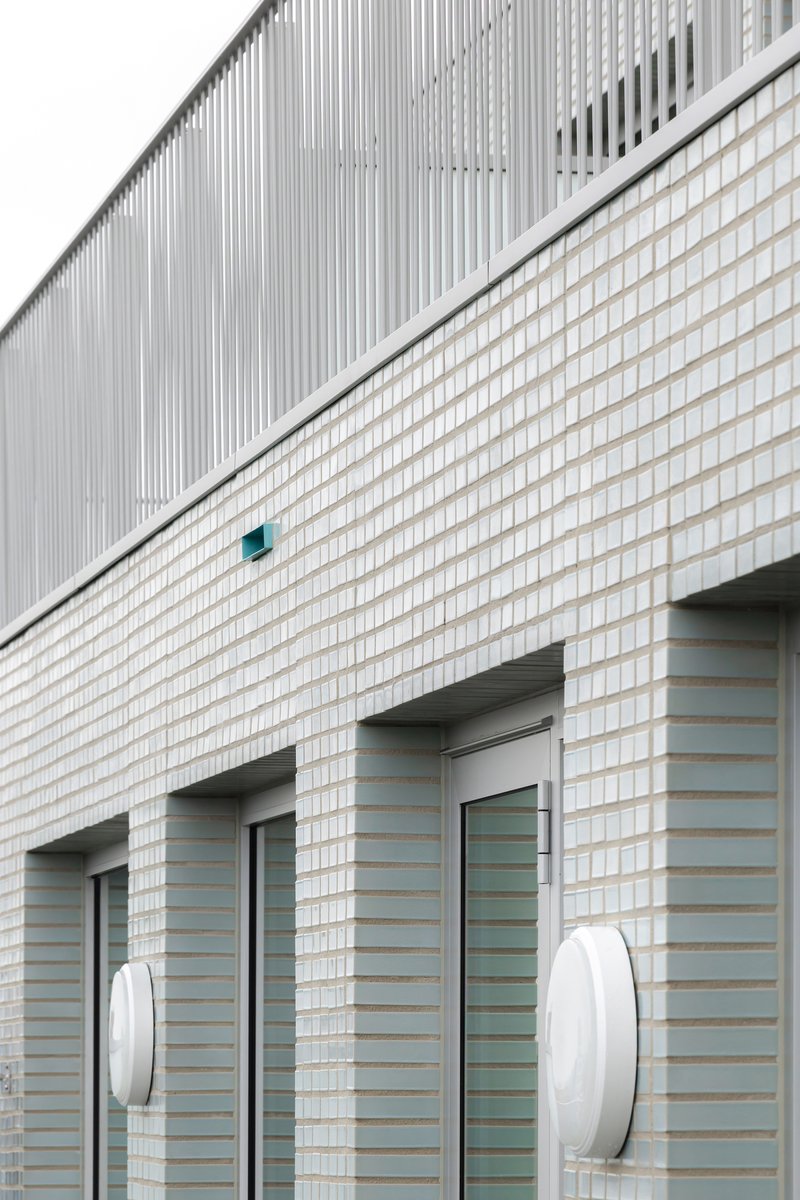 White brick facade with diagonal division line, entrance openings and circular wall-mounted light fixtures