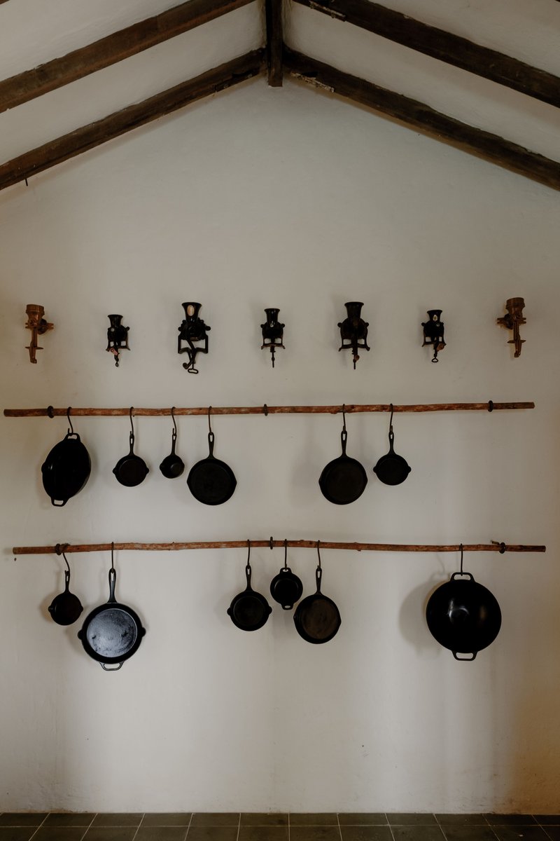 Vaulted interior wall with exposed timber beams, hanging cast iron pans and wall-mounted candle sconces