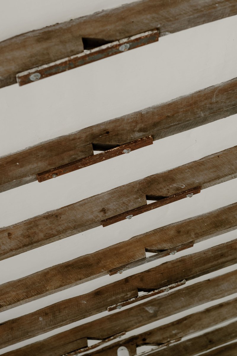 Close-up of weathered timber ceiling beams with exposed joinery and rust-stained metal connectors