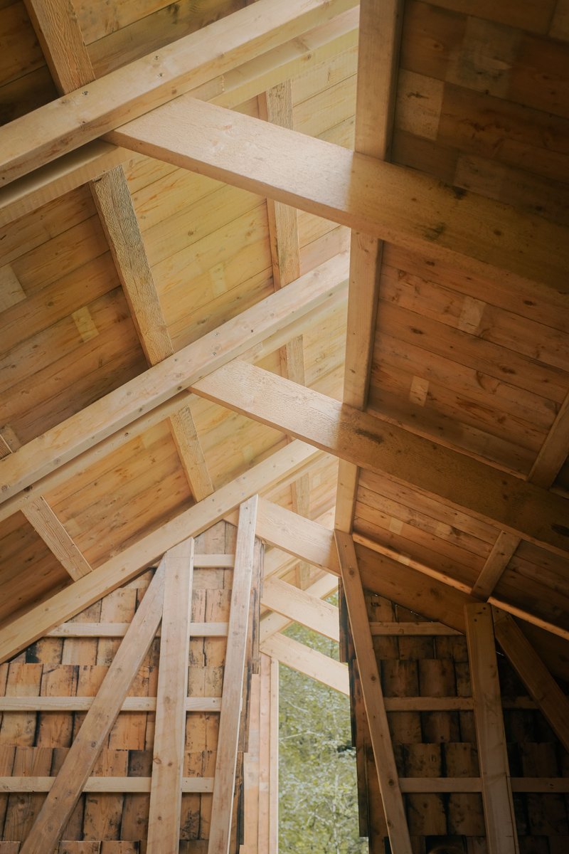 Upward view of exposed timber ceiling beams and rafters meeting at the roof ridge