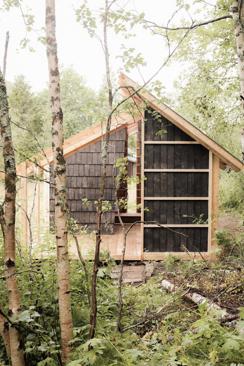 Gable end clad in dark shingles with large glazed opening framed by birch trees