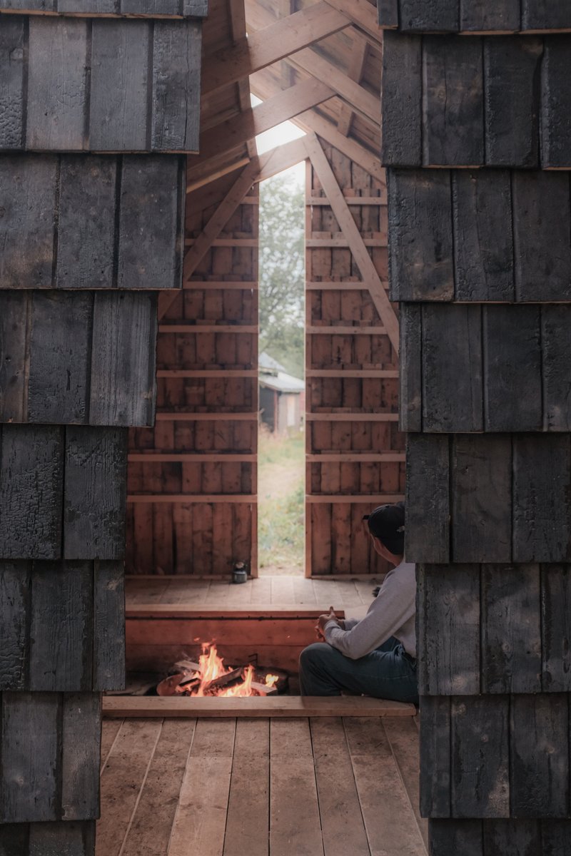 Interior view through open timber doors showing a person seated beside a fire pit