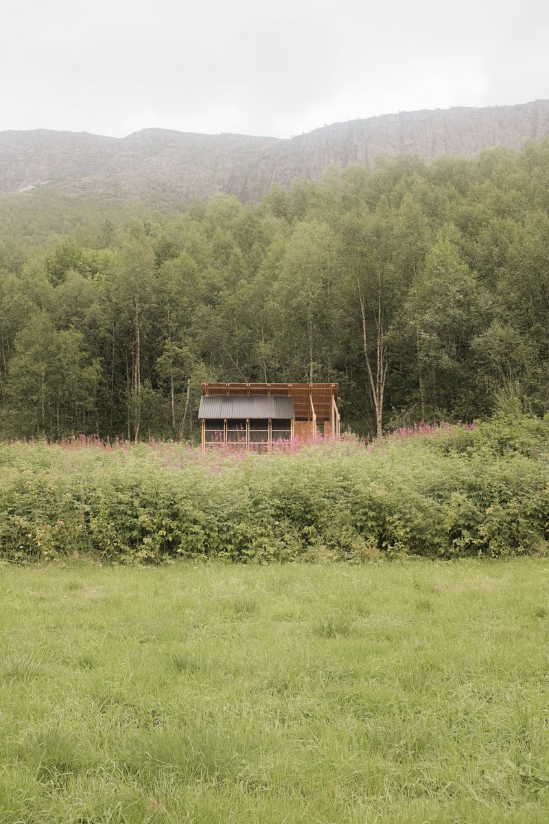 The pavilion across a wildflower meadow with forested mountains under overcast skies