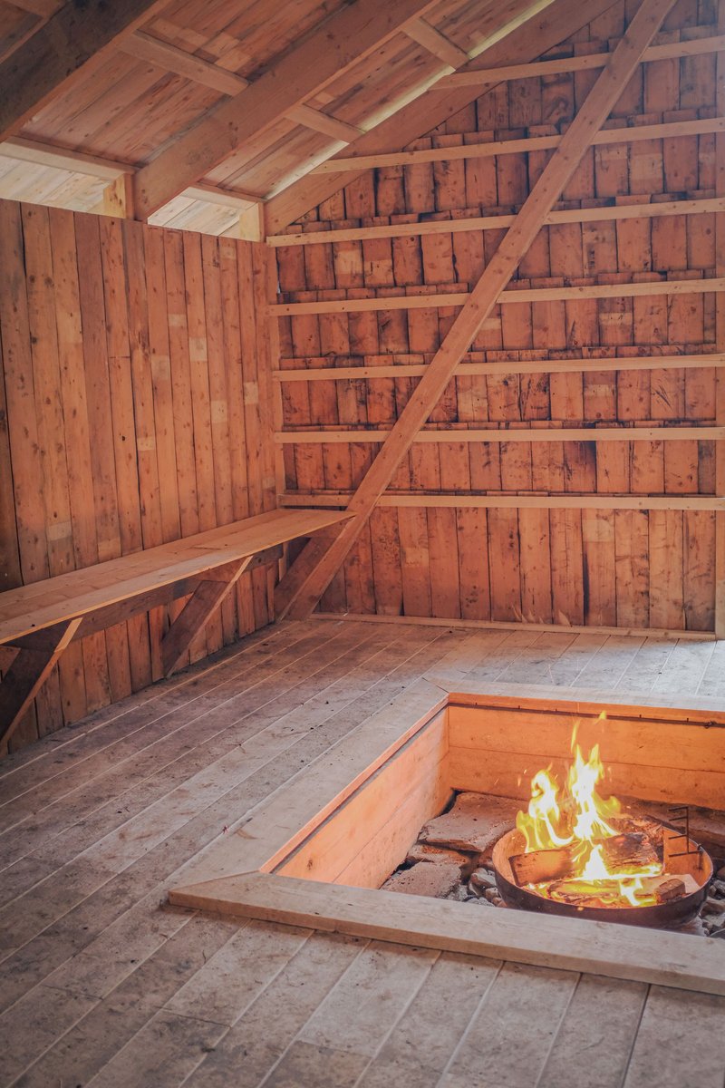 Interior timber sauna with exposed rafters, built-in benches, and sunken fire pit
