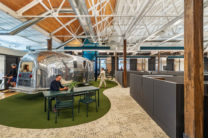 Open office interior with exposed white trusses, timber ceiling, transparent bubble pods and artificial turf flooring