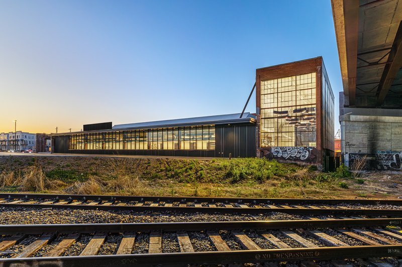 Glass-fronted facade with tower element viewed across railroad tracks at dusk