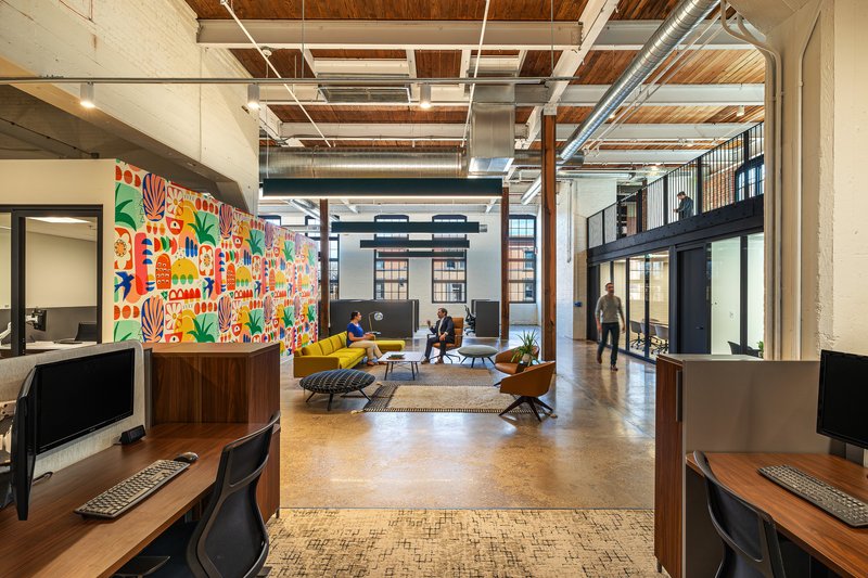 Open office lounge with exposed timber ceiling, pendant lights, and a colorful patterned mural wall