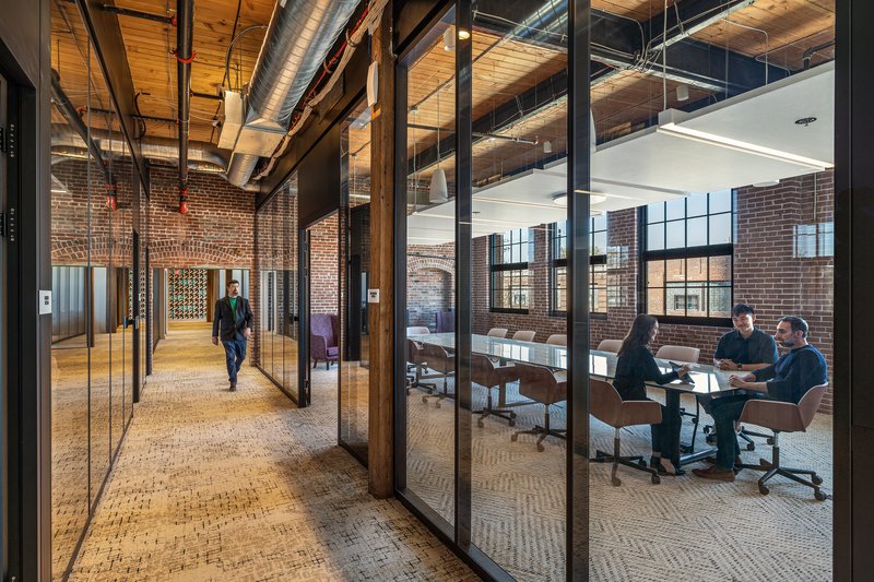 Glazed corridor with black steel frames alongside a conference room with exposed brick walls