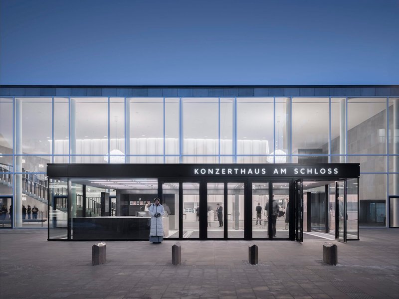 Ground-level entrance canopy with dark steel frame and glass doors facing the plaza