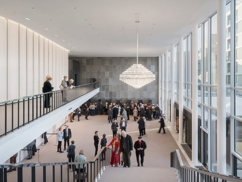 Double-height foyer with staircase and tiered chandelier as concertgoers gather below