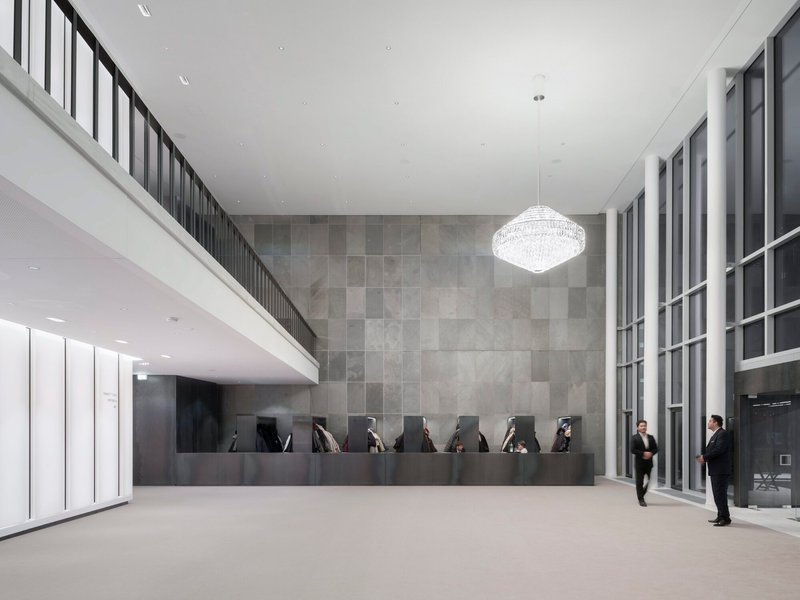 Reception desk with dark stone paneling beneath a mezzanine and crystal chandelier