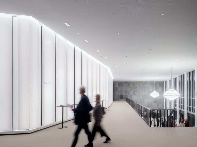 Upper-level corridor with vertical white panels along one wall and two blurred figures walking