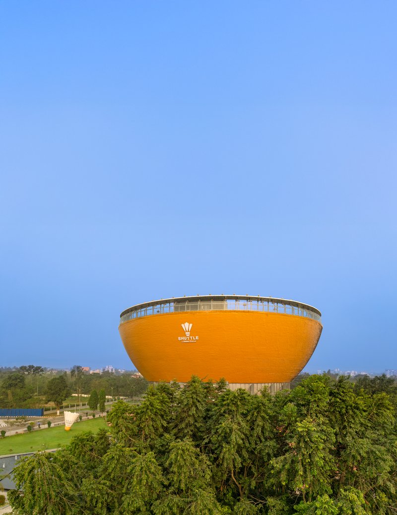 Exterior view of the elevated orange bowl-shaped volume rising above surrounding trees at dusk