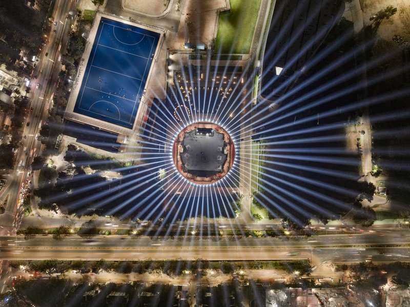 Aerial view at night showing radial light beams emanating from the circular structure