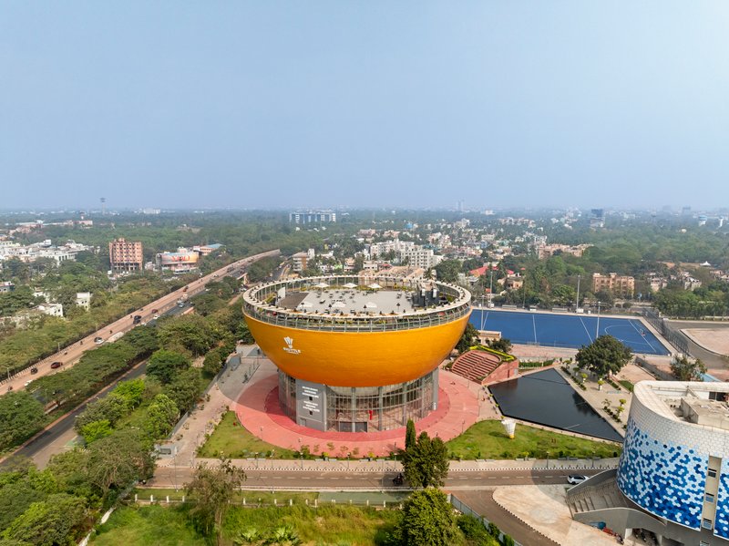 Aerial view of the bowl-shaped yellow volume with rooftop terrace overlooking surrounding roads and residential blocks