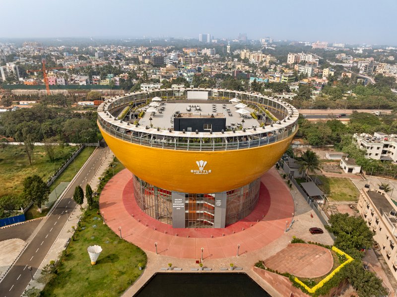 Elevated view of the circular building with yellow facade and pink plaza base surrounded by lawns and streets